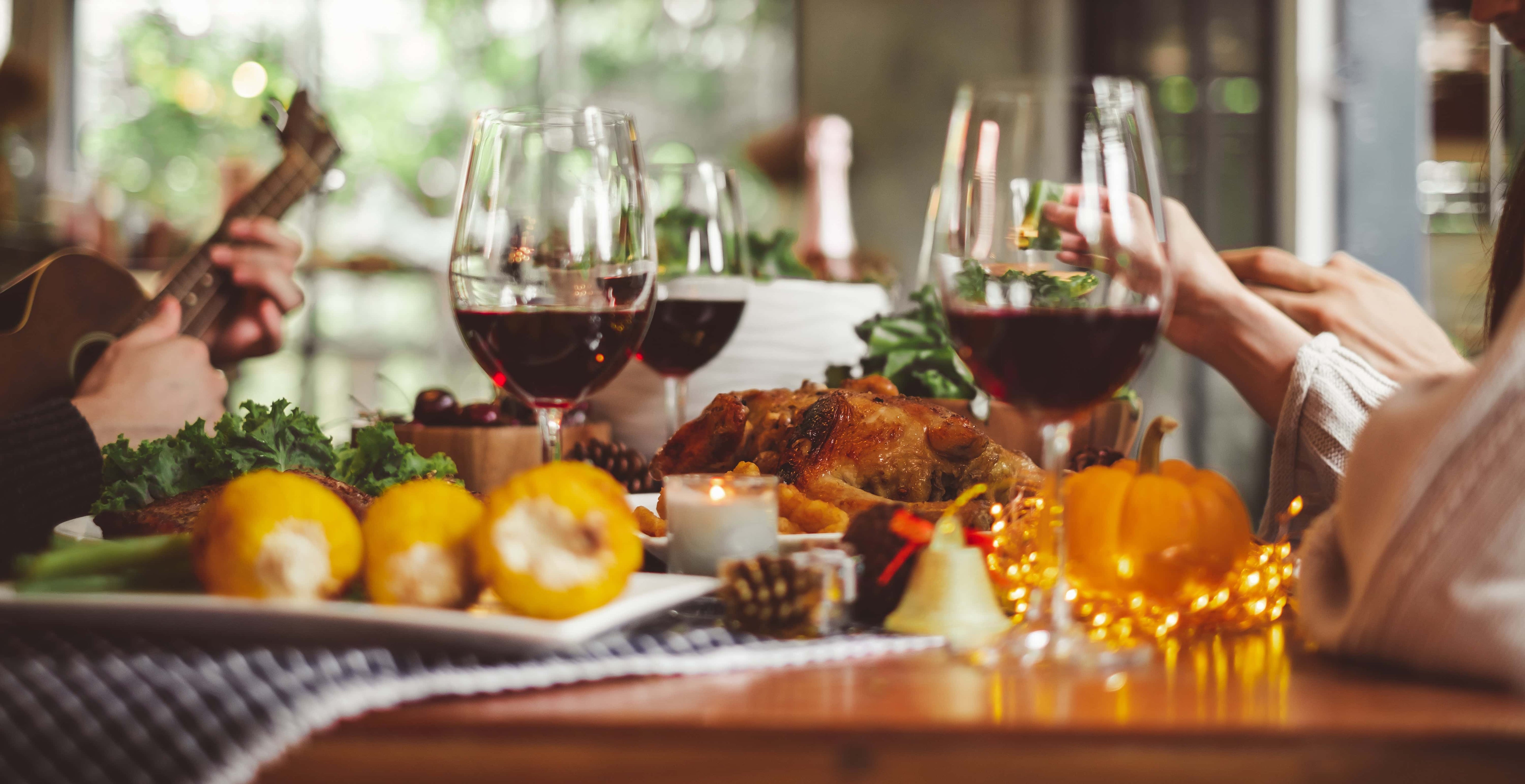 Festive Thanksgiving dinner with roast turkey, red wine, corn, and pumpkins on a cozy autumn table setting.