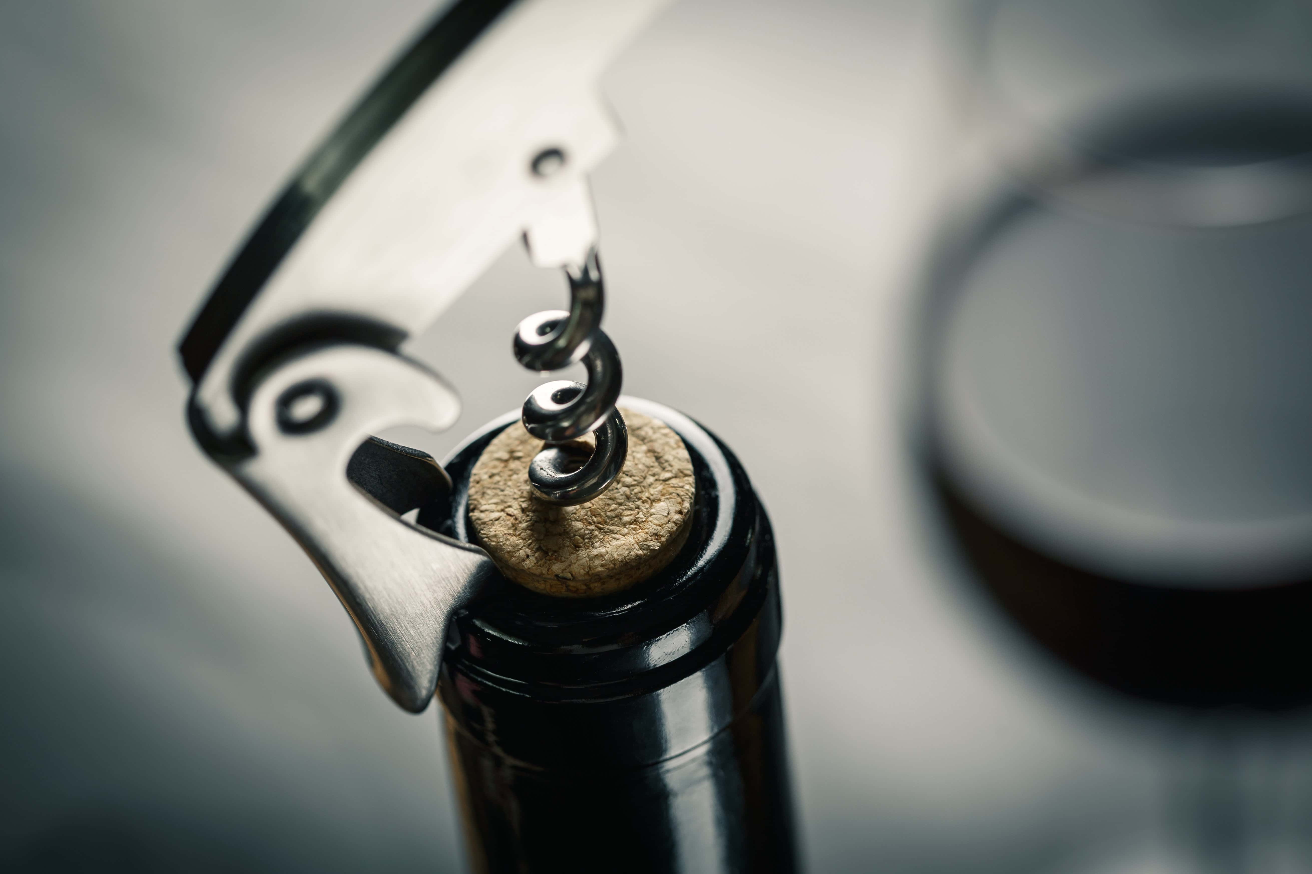 How to open wine without a corkscrew - corkscrew opening a wine bottle with blurred wine glass.