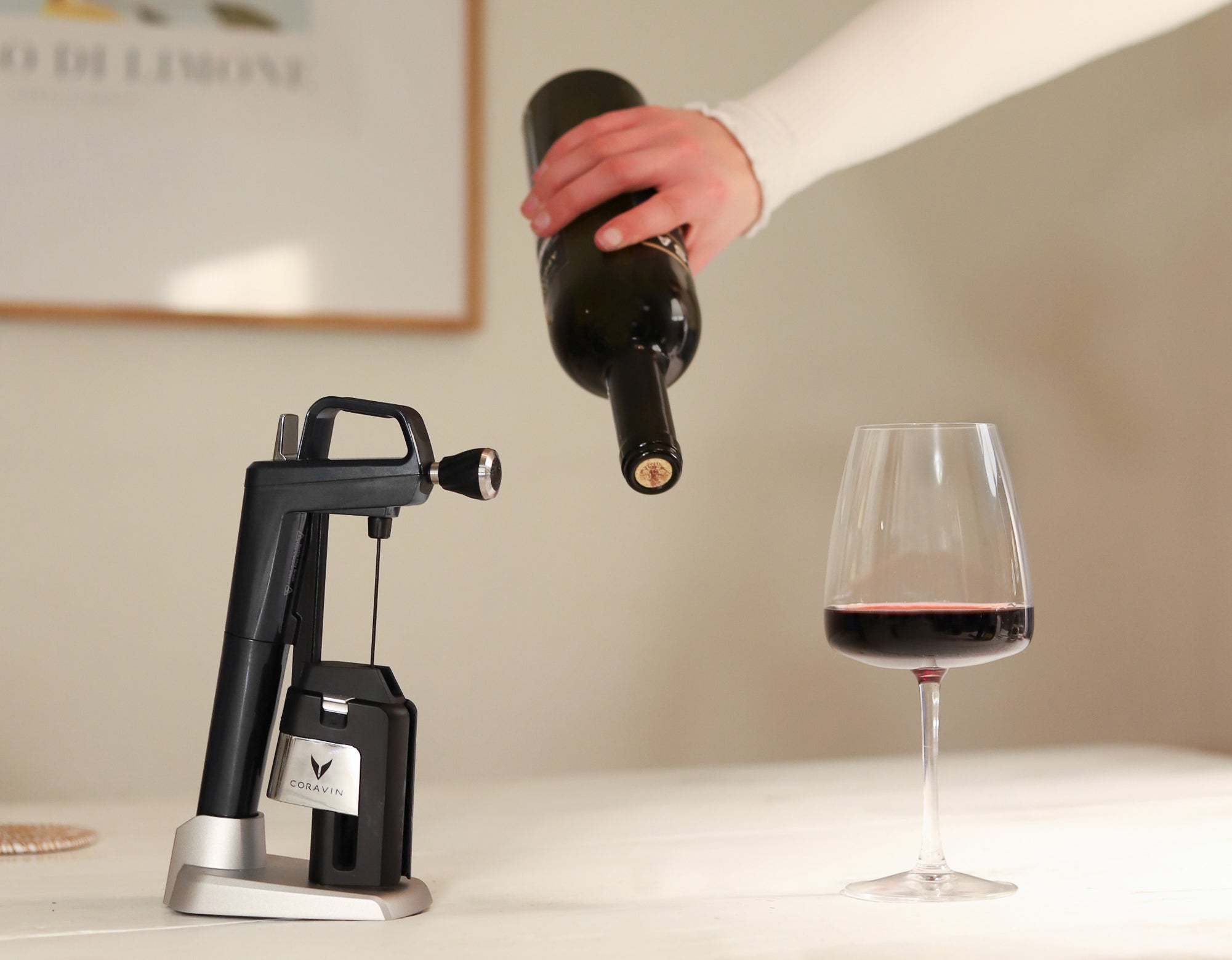 Hand pouring red wine with a Coravin wine preservation system on the table, demonstrating how to serve wine without removing the cork.