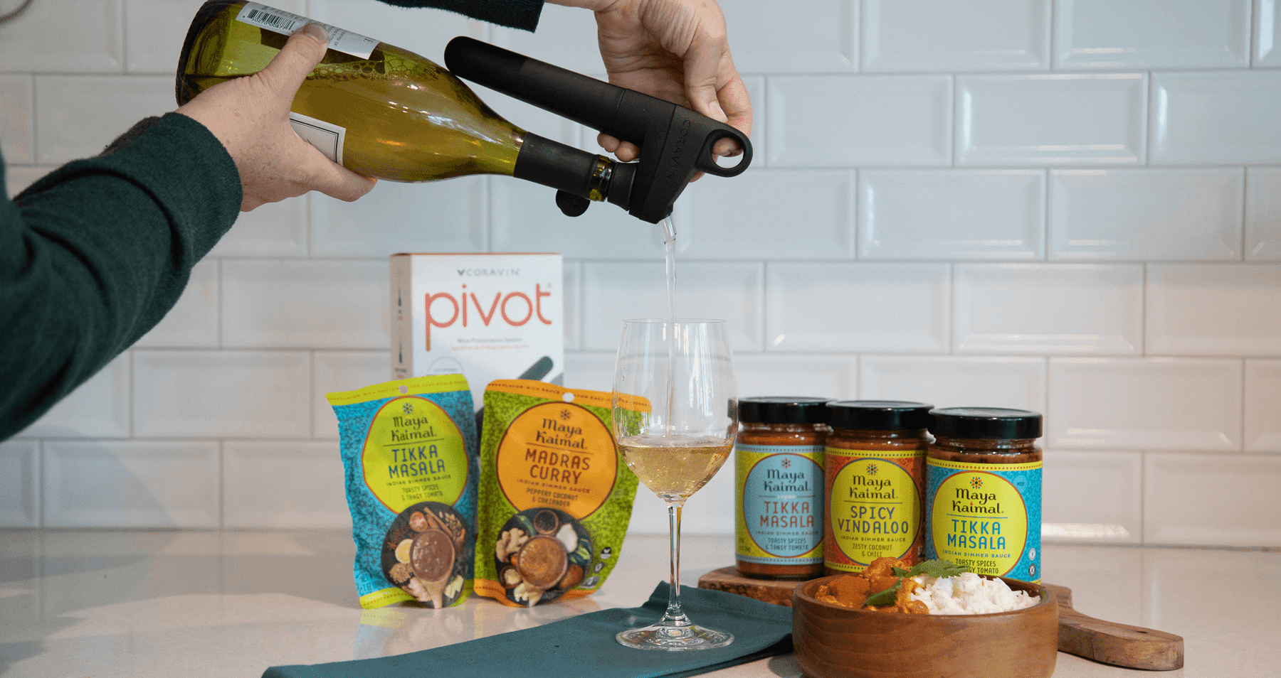 Pouring white wine with Coravin Pivot beside Maya Kaimal Indian sauces, highlighting wine and Indian food pairing in a modern kitchen.