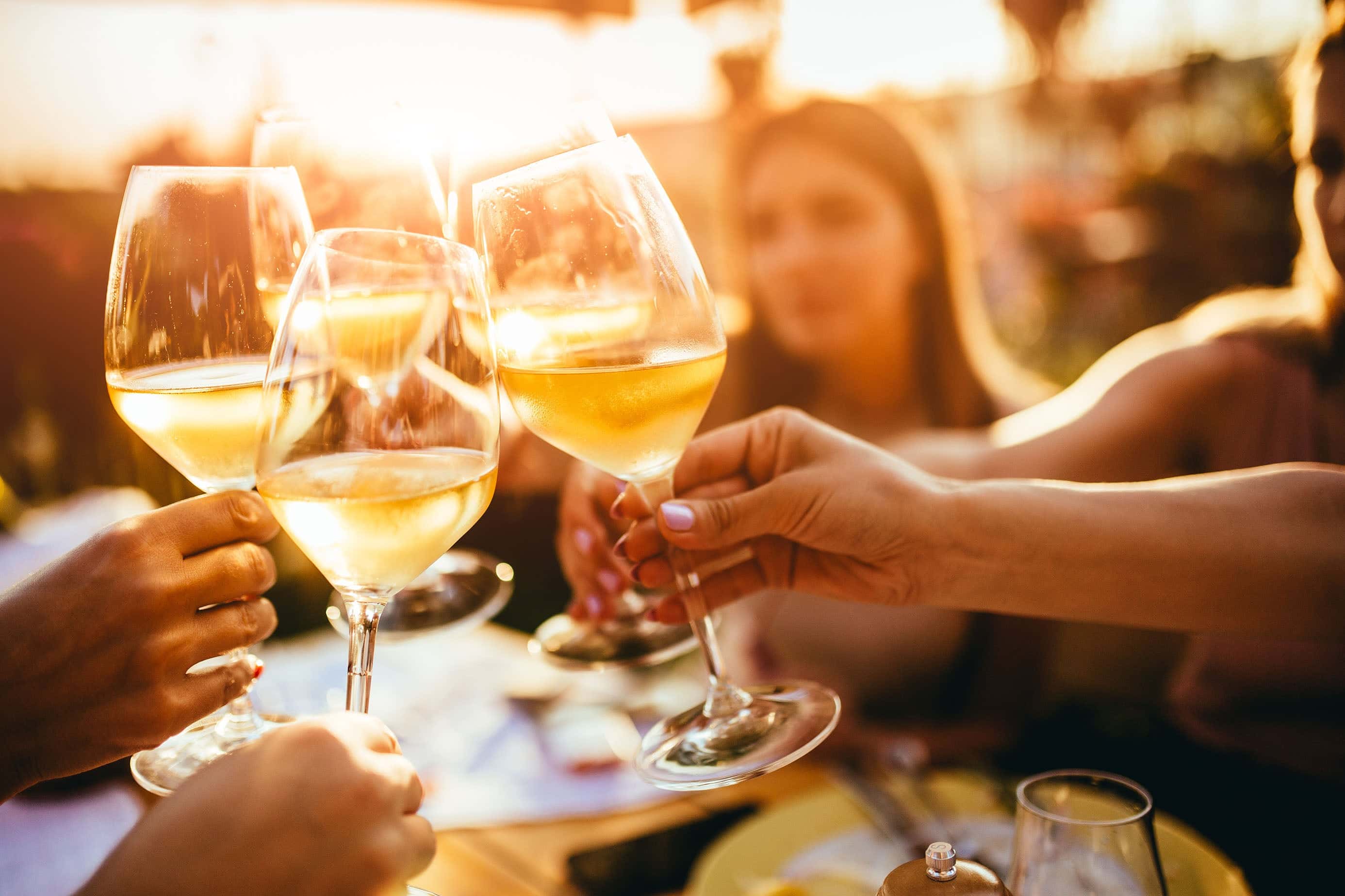 Group of friends toasting with chilled white wine glasses during a golden hour outdoor gathering, celebrating in a relaxed summer atmosphere.