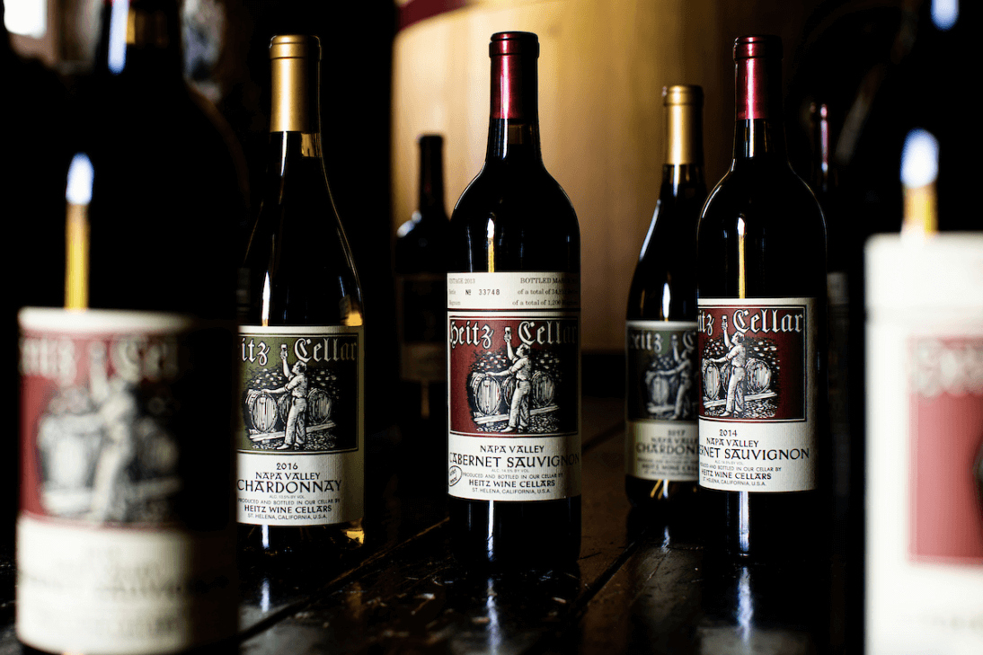 Assorted bottles of Heitz Cellar Napa Valley wines, including Cabernet Sauvignon and Chardonnay, displayed on a dark wooden surface with warm ambient lighting.