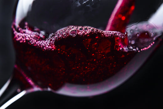 Close-up of red wine swirling in a glass with visible bubbles and reflections, highlighting texture, color, and alcohol content.