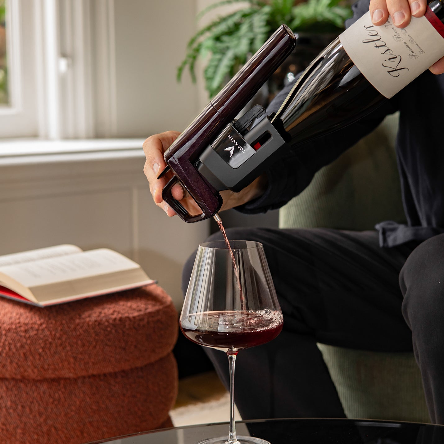 Person pouring red wine from a bottle with coravin timeless six into a glass in a cozy indoor setting.