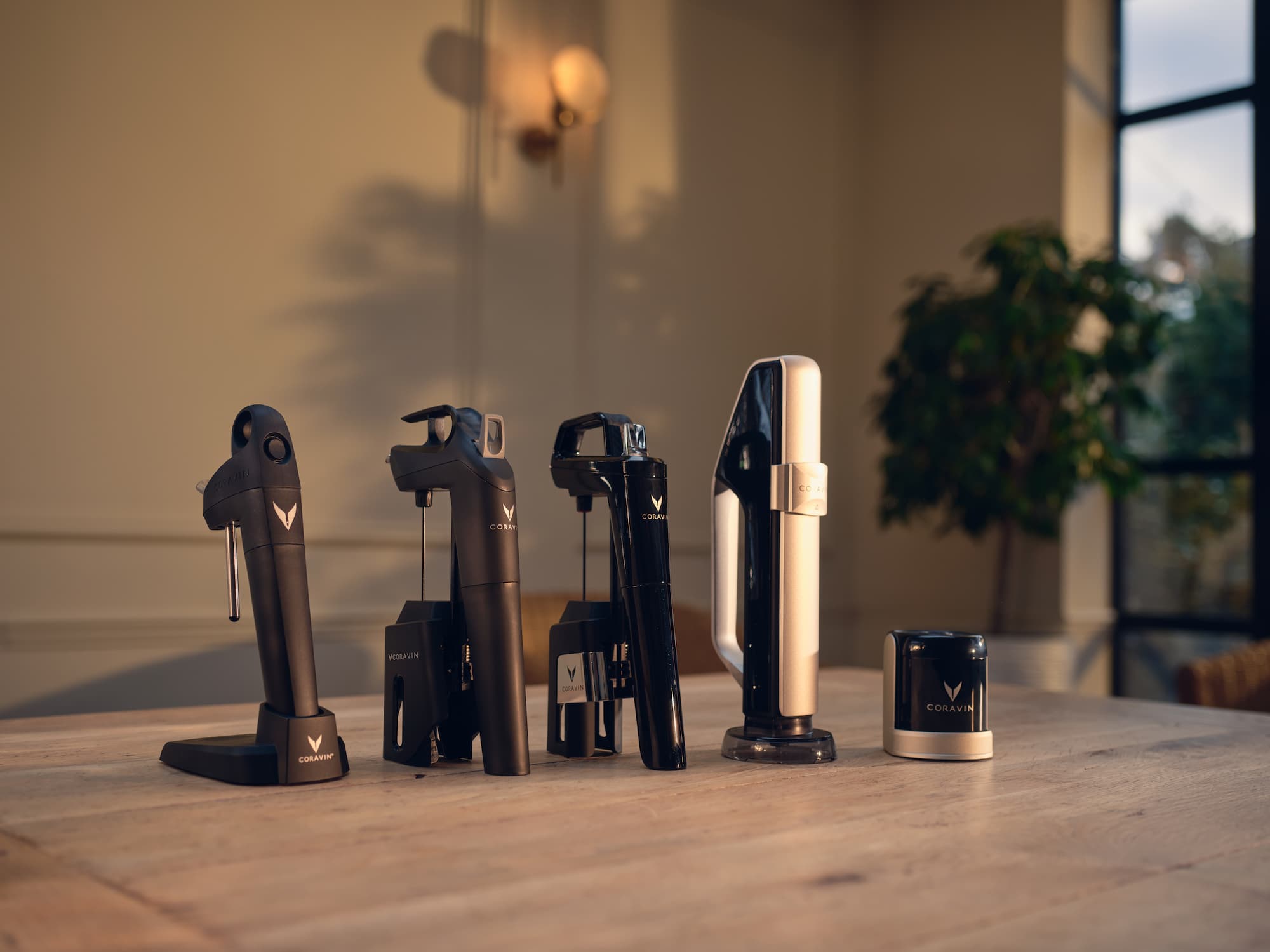 All Coravin wine systems displayed on a wooden table in a warmly lit room