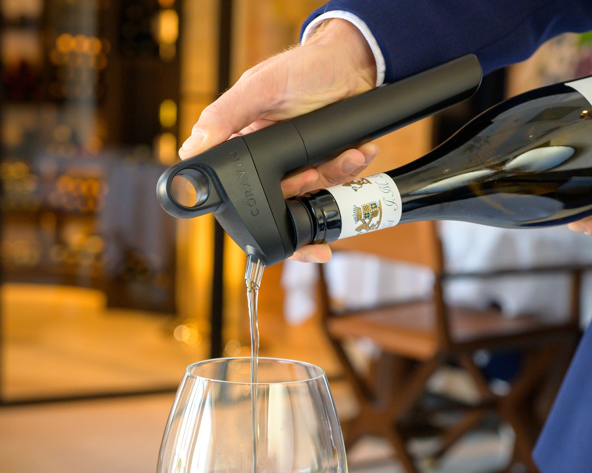 Person pouring white wine from a bottle into a glass in a restaurant setting.