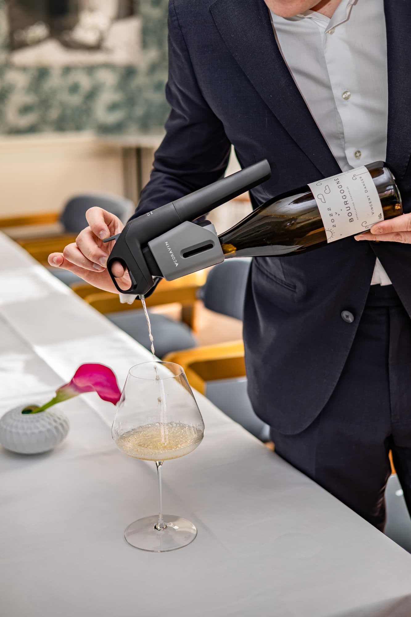 A person uses a Coravin wine preservation system to pour white wine from a bottle
